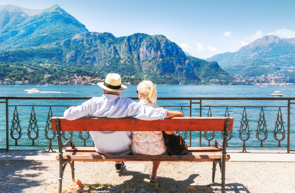 A senior couple sit on a bench looking at Lake Como in Italy