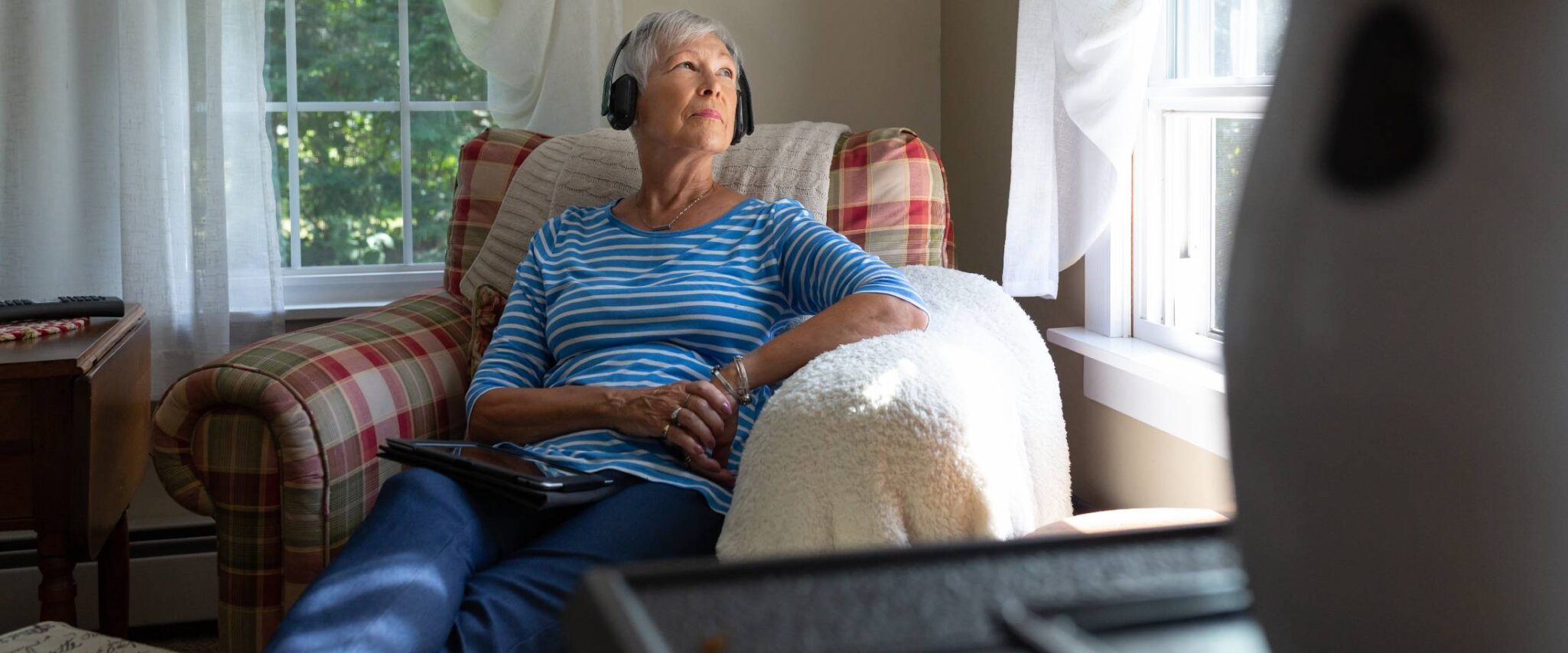 senior lady listening to music with headphones on while looking out a window