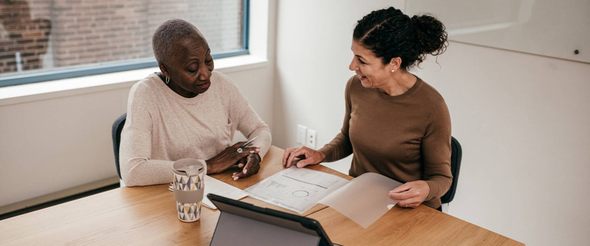 a middle aged woman helps an elderly woman with paperwork at a table