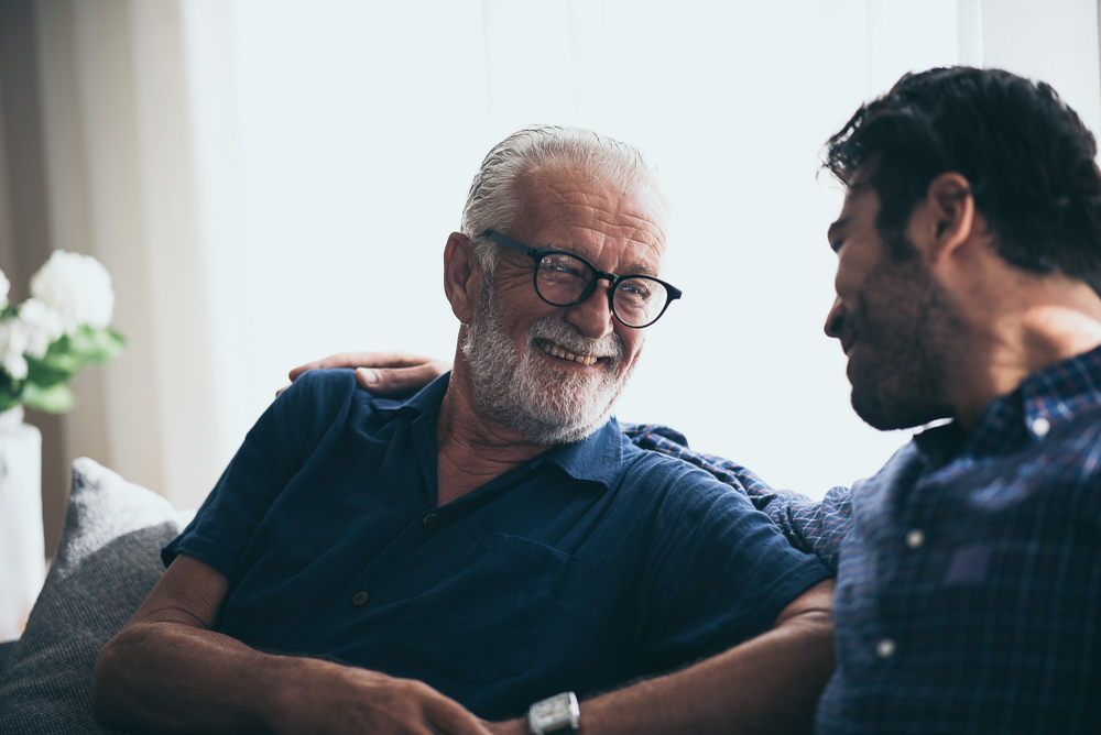 A senior man and his son talk while sitting on the sofa