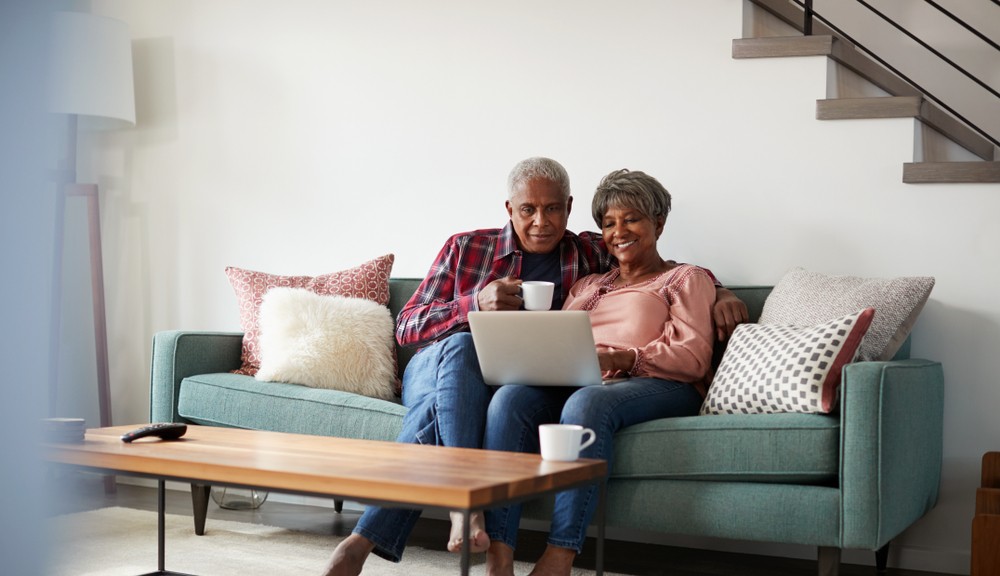 senior couple sitting on a couch while using a laptop