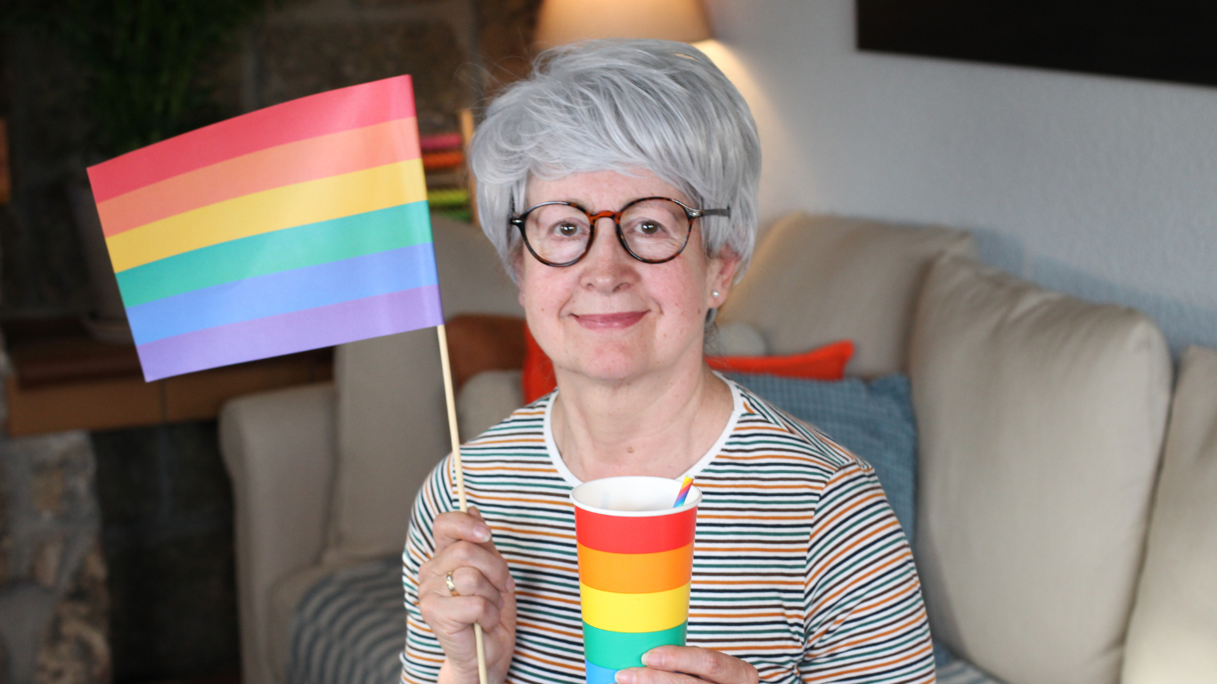 Blog Images – 2025-07-29T081621.034 Senior smiling and holding a rainbow cup and a Pride flag