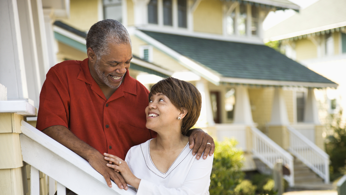 A senior woman and a senior man stand outside their home