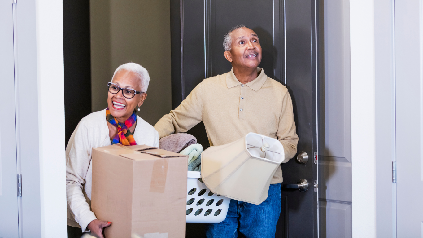 Senior couple holding moving boxes while walking through front door