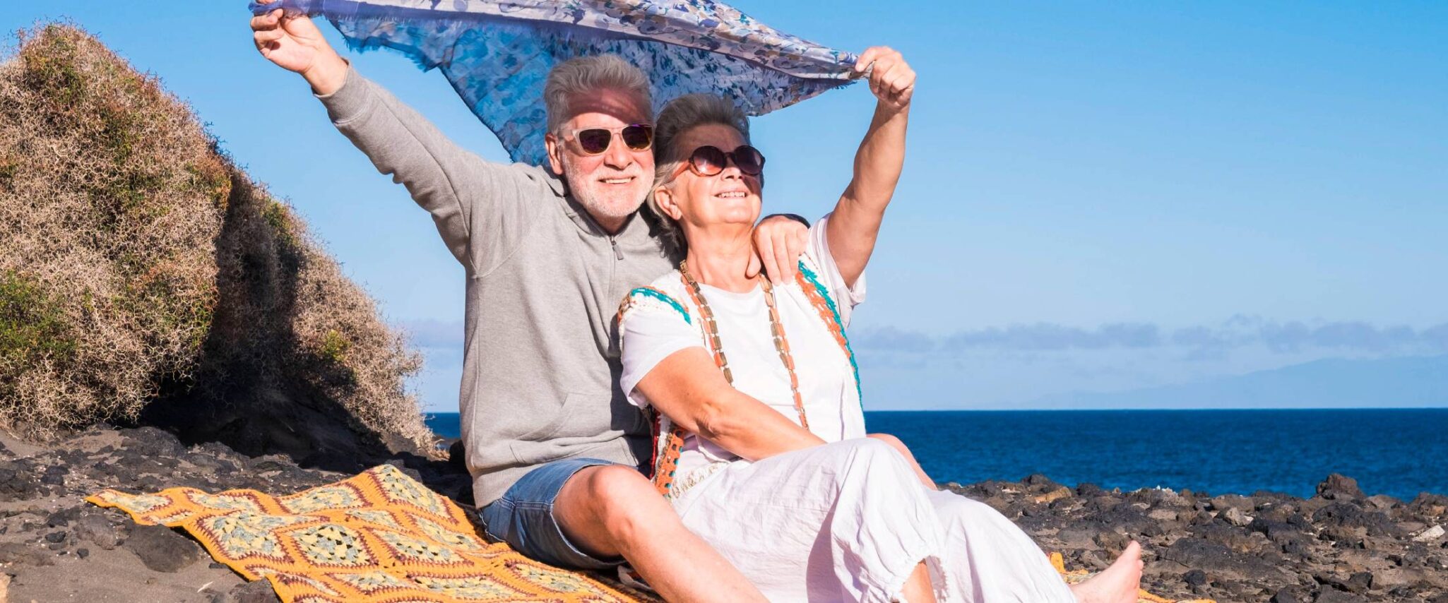 senior couple sitting in the sun on the beach on a beach towel