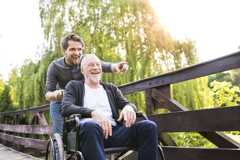 Happy son walking with disabled father in wheelchair at park.