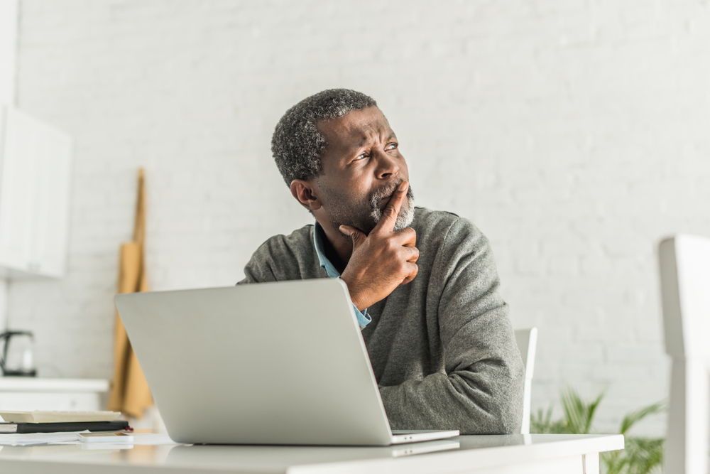 Thoughtful senior man looking away while using laptop