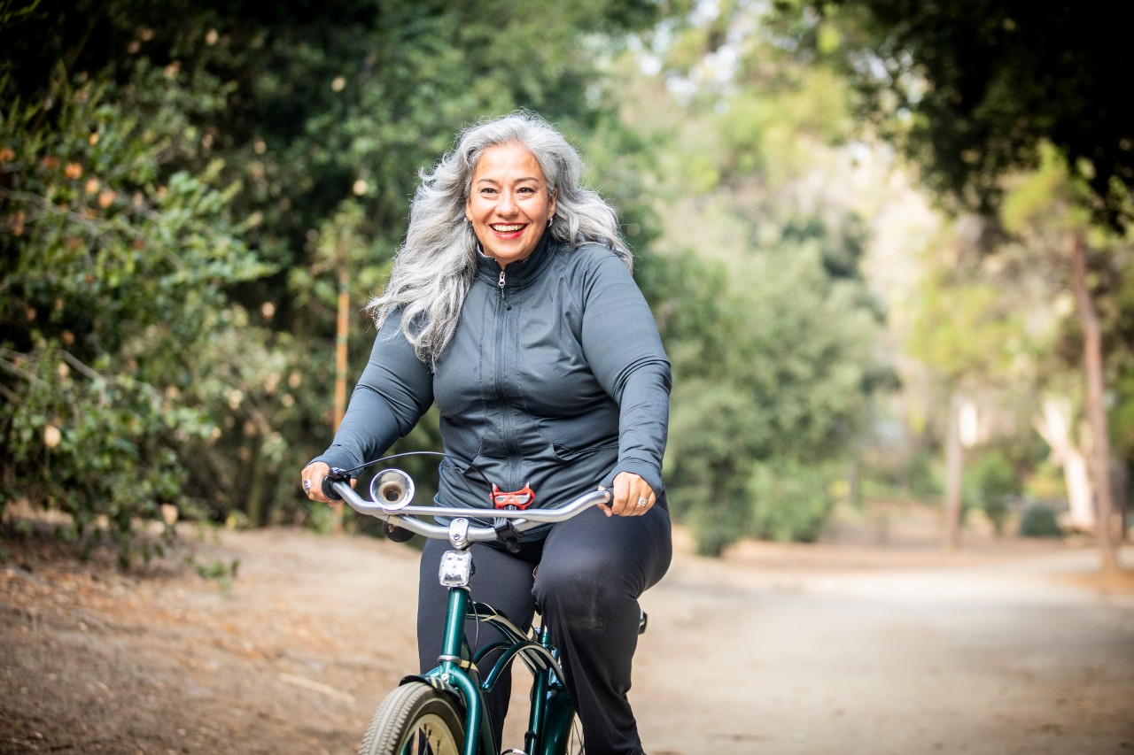 An older woman rides her bike on a forested path