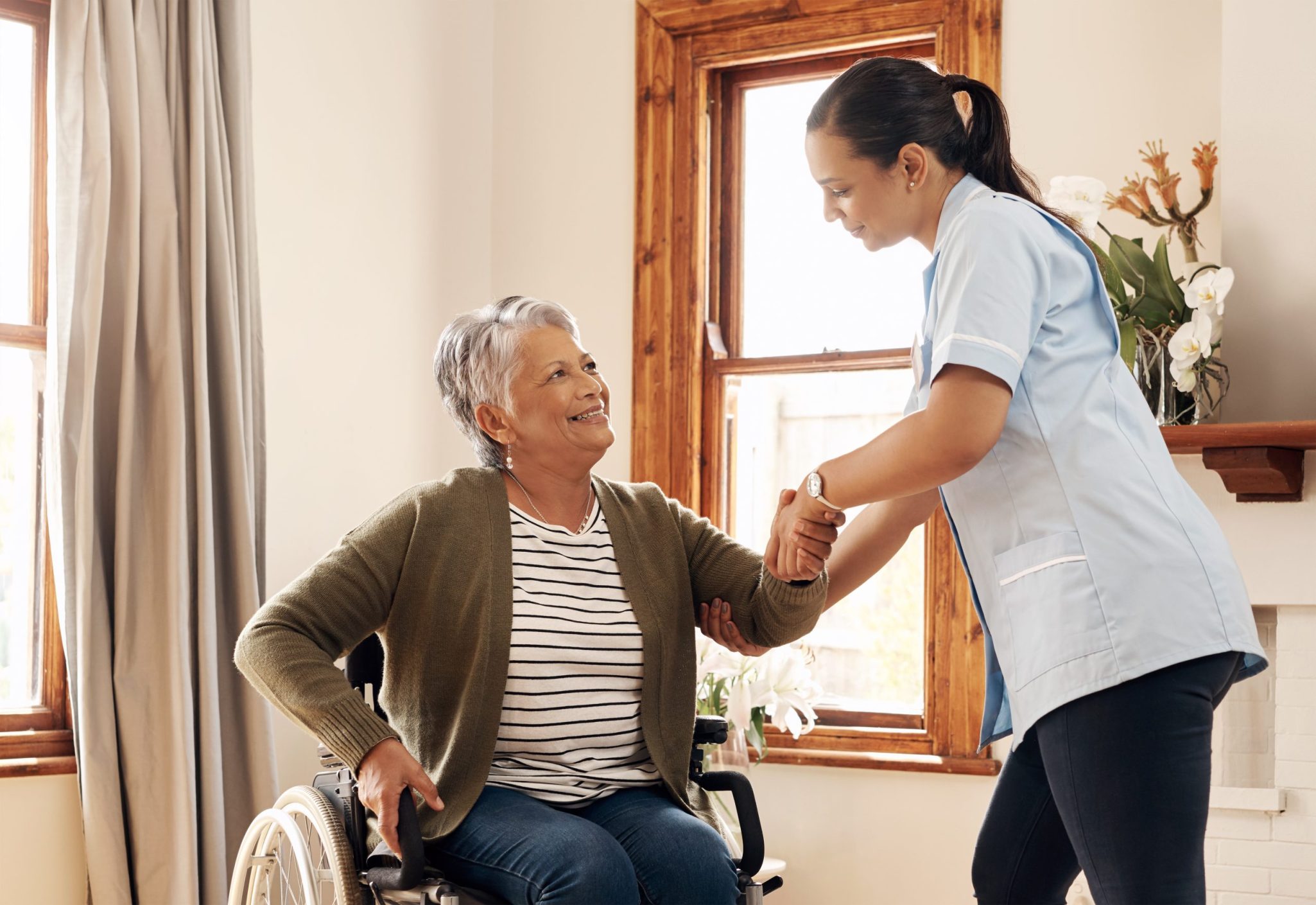 Senior woman in wheelchair receiving assistance from female nurse
