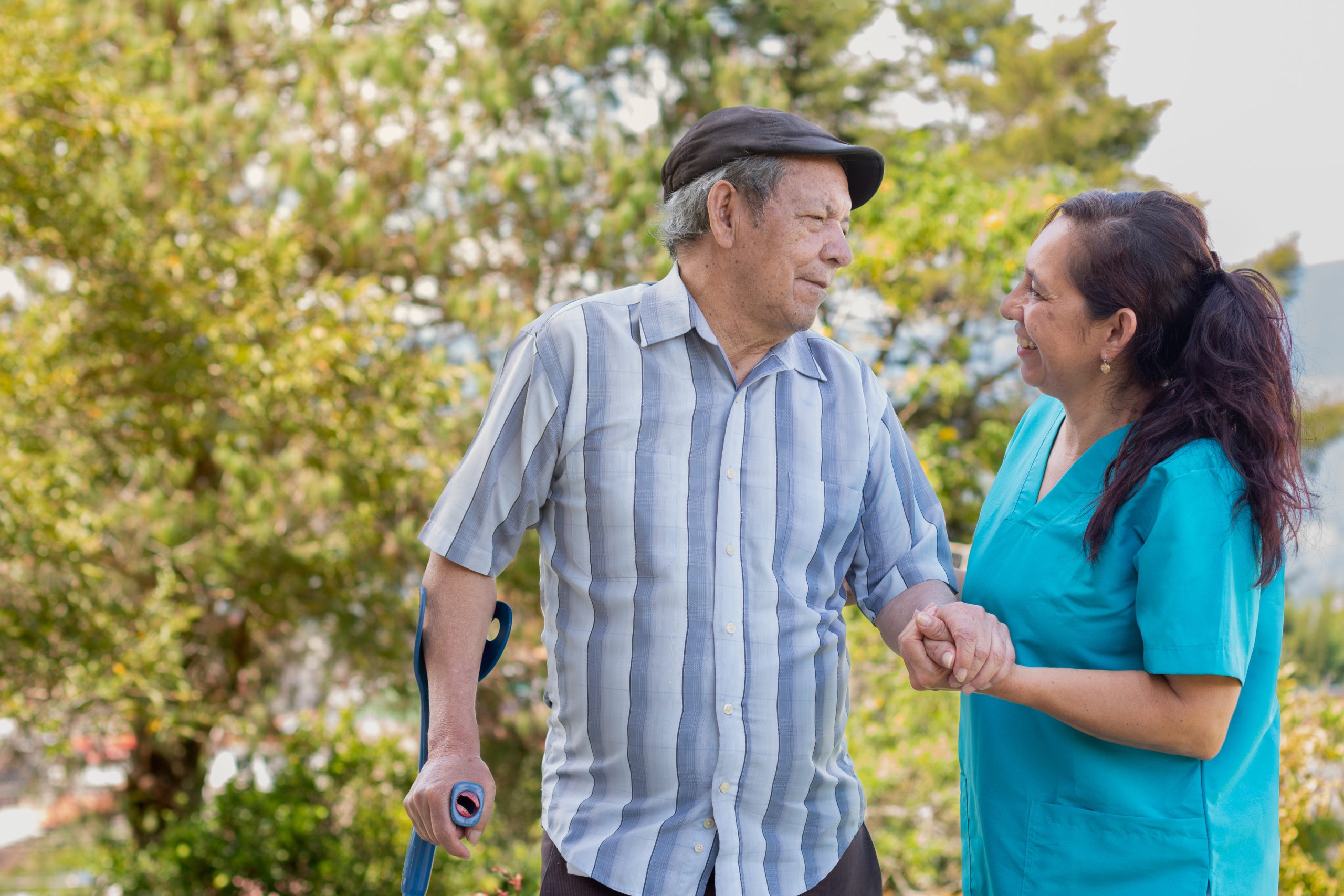 Senior man with cane holding hand of female nurse in park