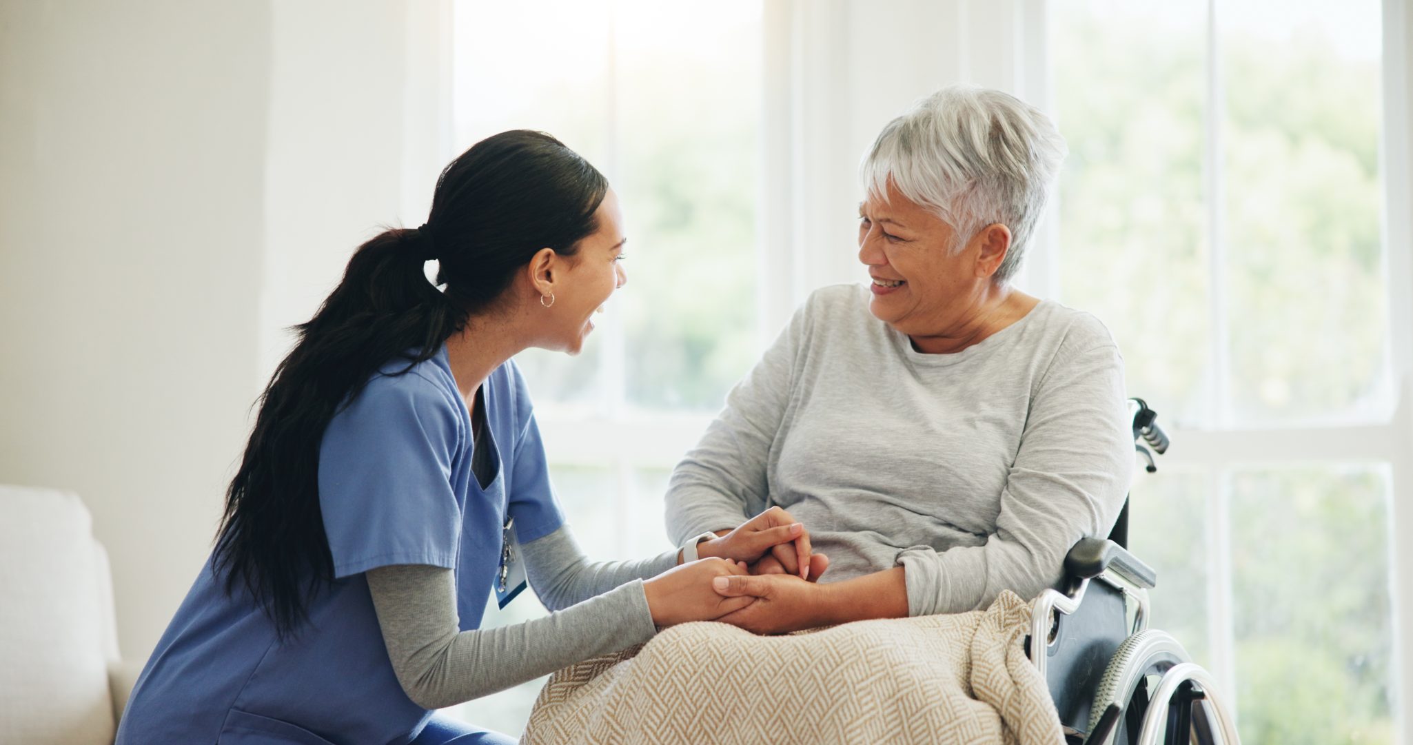 Smiling senior woman in wheelchair holding hands with female nurse